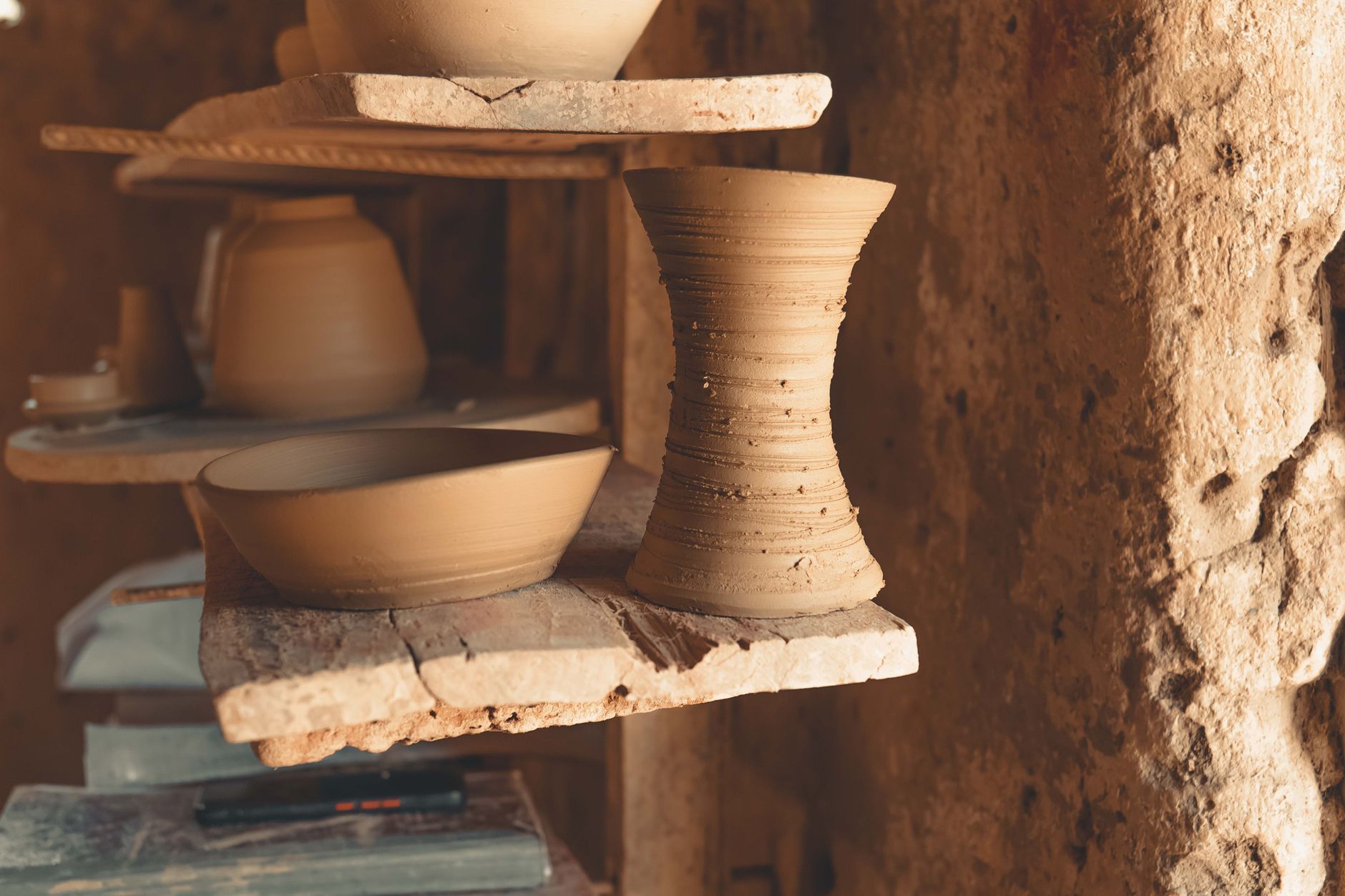 Handmade ceramic bowls and vases on a rustic shelf