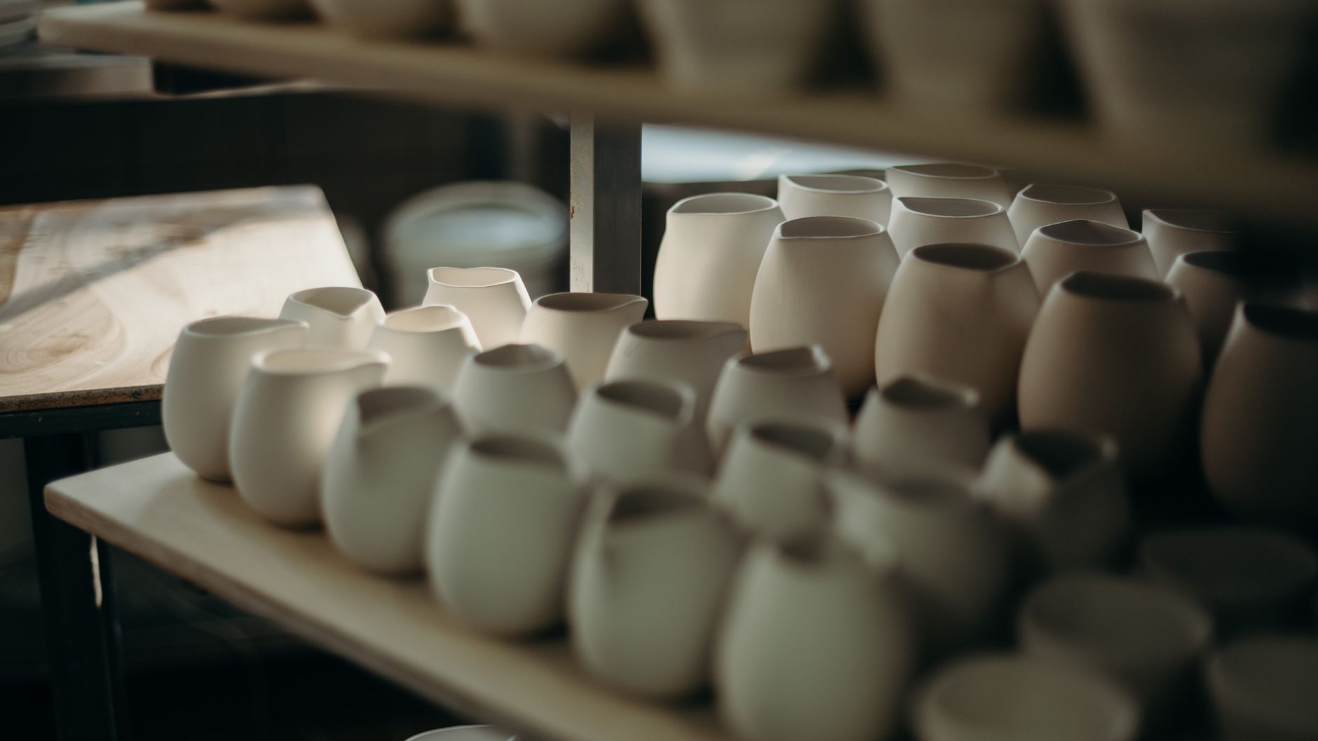 Handmade ceramic pots and mugs displayed on wooden shelves