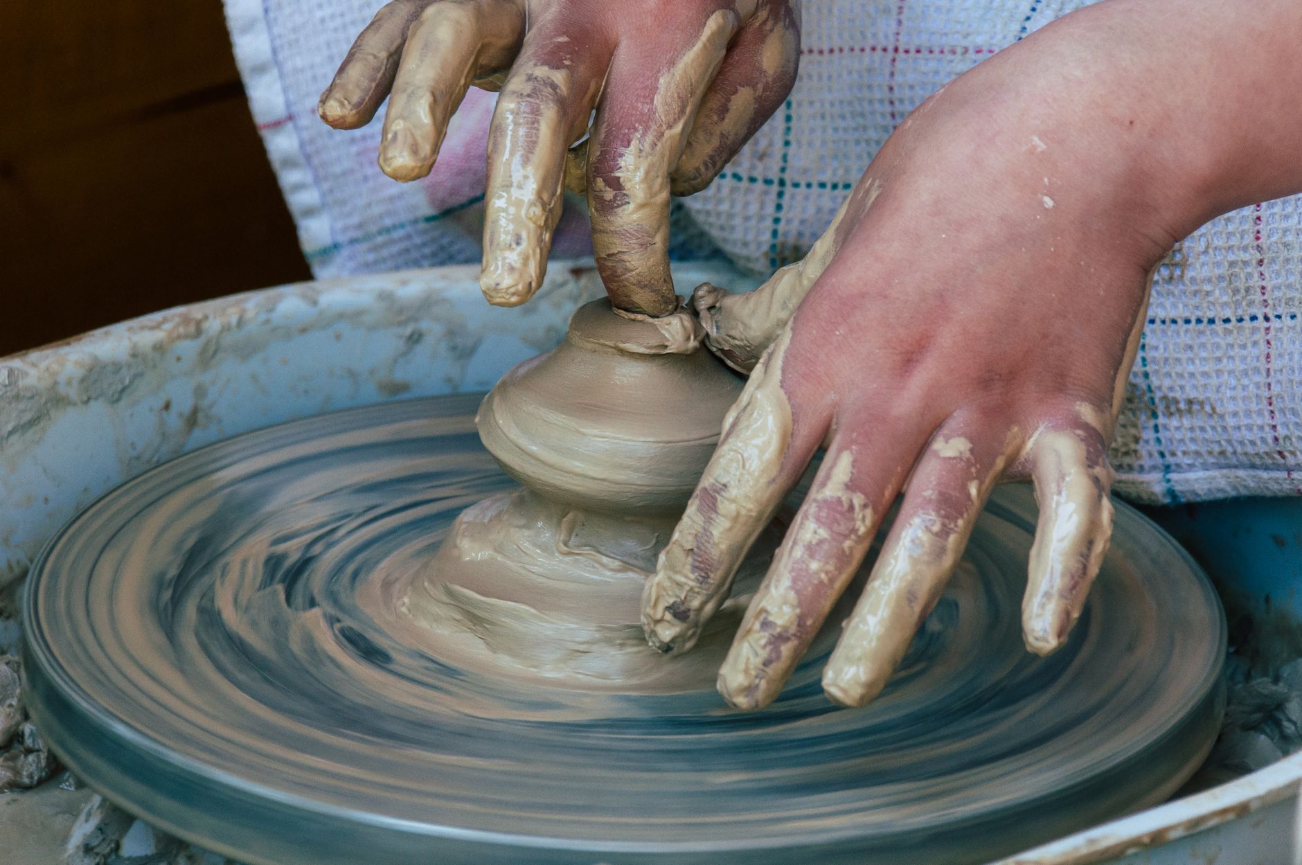 Hands shaping a clay pot on a pottery wheel